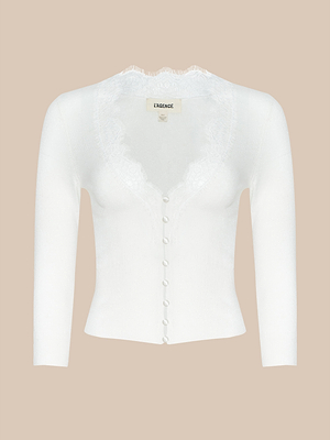 The Eluna Cardigan Top is a white, lightweight knit with long sleeves, button-up front, fitted silhouette, and lace-trimmed V-neckline, shown on a neutral beige background.
