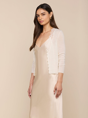 A woman with long brown hair wears the Eluna Cardigan Top over a light beige satin slip dress, standing against a plain beige background.
