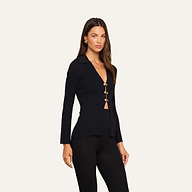 A woman stands against a plain light background wearing the Kaye Cardigan Top—a fitted black knit cardigan with gold buttons—paired with matching black pants. Her hair is worn loose, she accessorizes with gold earrings, and gazes confidently toward the camera.