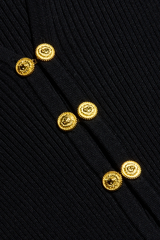 Close-up of six textured gold buttons arranged vertically on black, ribbed knit fabric, showcasing their shiny, detailed surface and the Kaye Cardigan Top’s elegant, structured design—perfect for elevating any travel set or pairing seamlessly with your favorite separates.