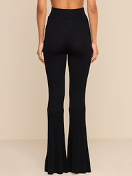 A person stands facing away, wearing the Conan Knit Pant in black. These high-rise knit pants are fitted through the thigh and flare out at the bottom. The background is plain white.