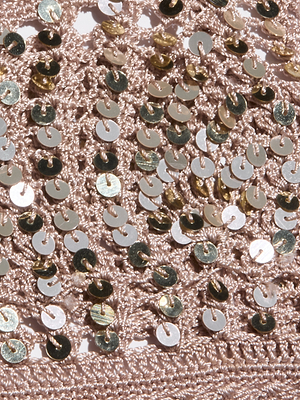 Close-up of the Taline Crocheted Bralette shows light pink crochet fabric adorned with shiny round silver and gold sequins, creating a textured, reflective surface—ideal for a statement top or standout summer look.