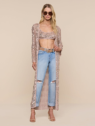 A woman wearing sunglasses, a sequin crop top, ripped blue jeans, heeled sandals, and the Sanya Crocheted Cardigan stands against a plain white background—perfect as a chic vacation outfit or swimsuit cover up.