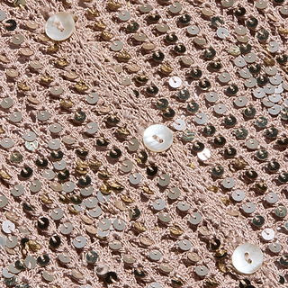 Close-up of the Sanya Crocheted Cardigan in pink, featuring shiny sequins and a scattering of small, round white buttons—perfect for adding a dazzling touch as a swimsuit cover-up on your next summer vacation.