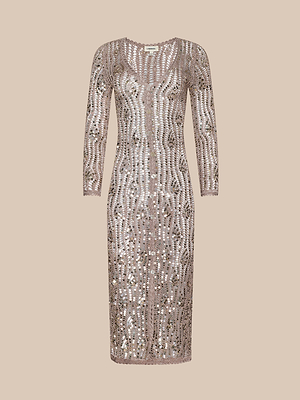 The Sanya Crocheted Cardigan is a knee-length, long-sleeved nude cover-up with intricate crochet details, perfect for vacations or as a glamorous swimsuit layer, shown against a neutral beige background.