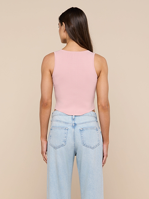 A woman with long brown hair faces away, wearing the sleeveless pink Dove Knit Corset Top and light blue high-waisted jeans against a plain beige background.