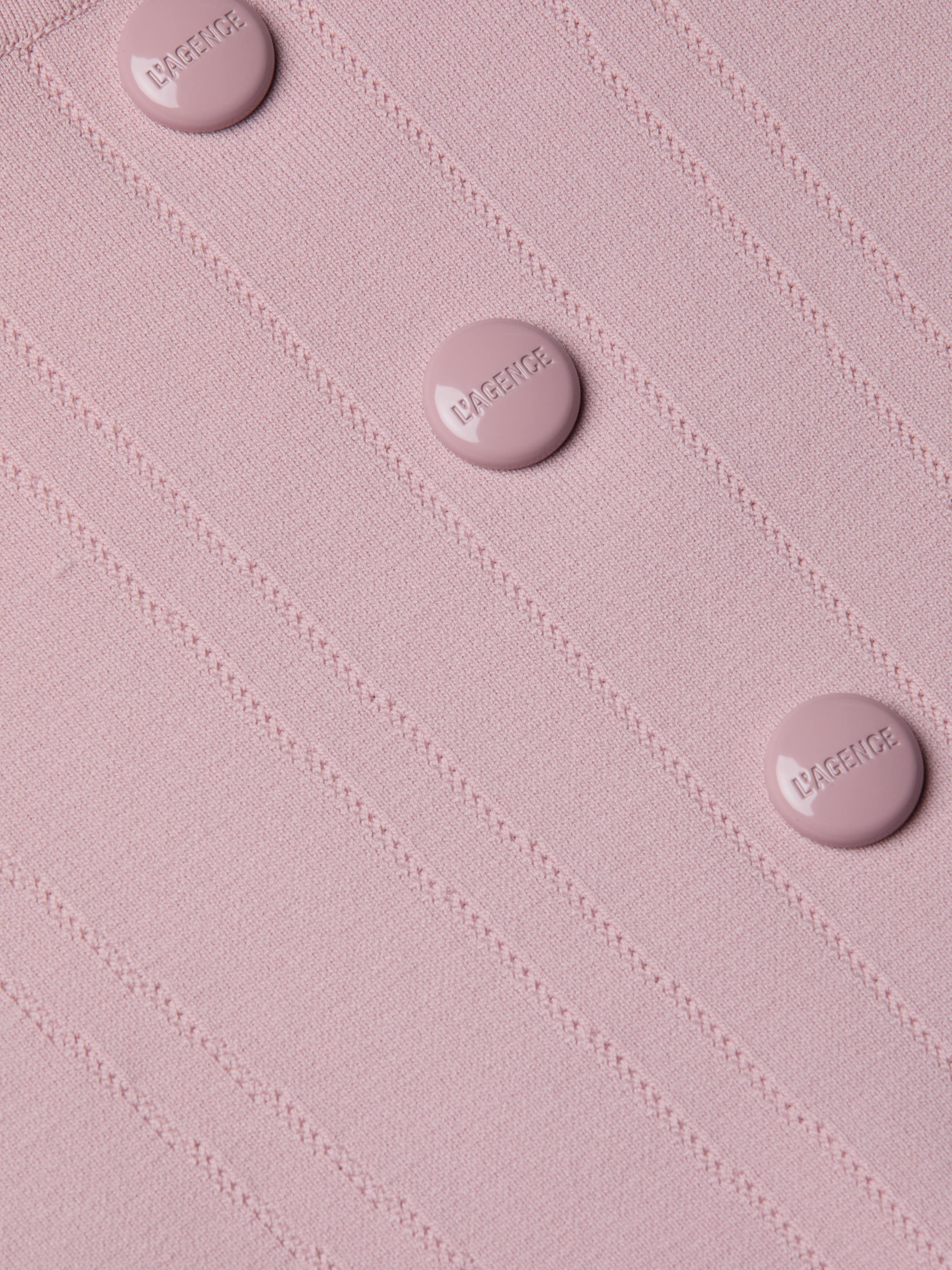 Close-up of the Dove Knit Corset Top, a light pink fitted piece featuring a ribbed power knit texture and four round buttons embossed with “LAGENCE” arranged in a neat vertical line. The design is finished with a subtle curved hemline.