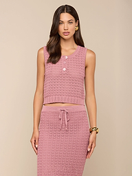 Una donna indossa la canottiera Carven Pointelle Knit Tank in rosa testurizzato con bottoni, abbinata a una gonna a vita alta con coulisse e accessori dorati, su uno sfondo beige.