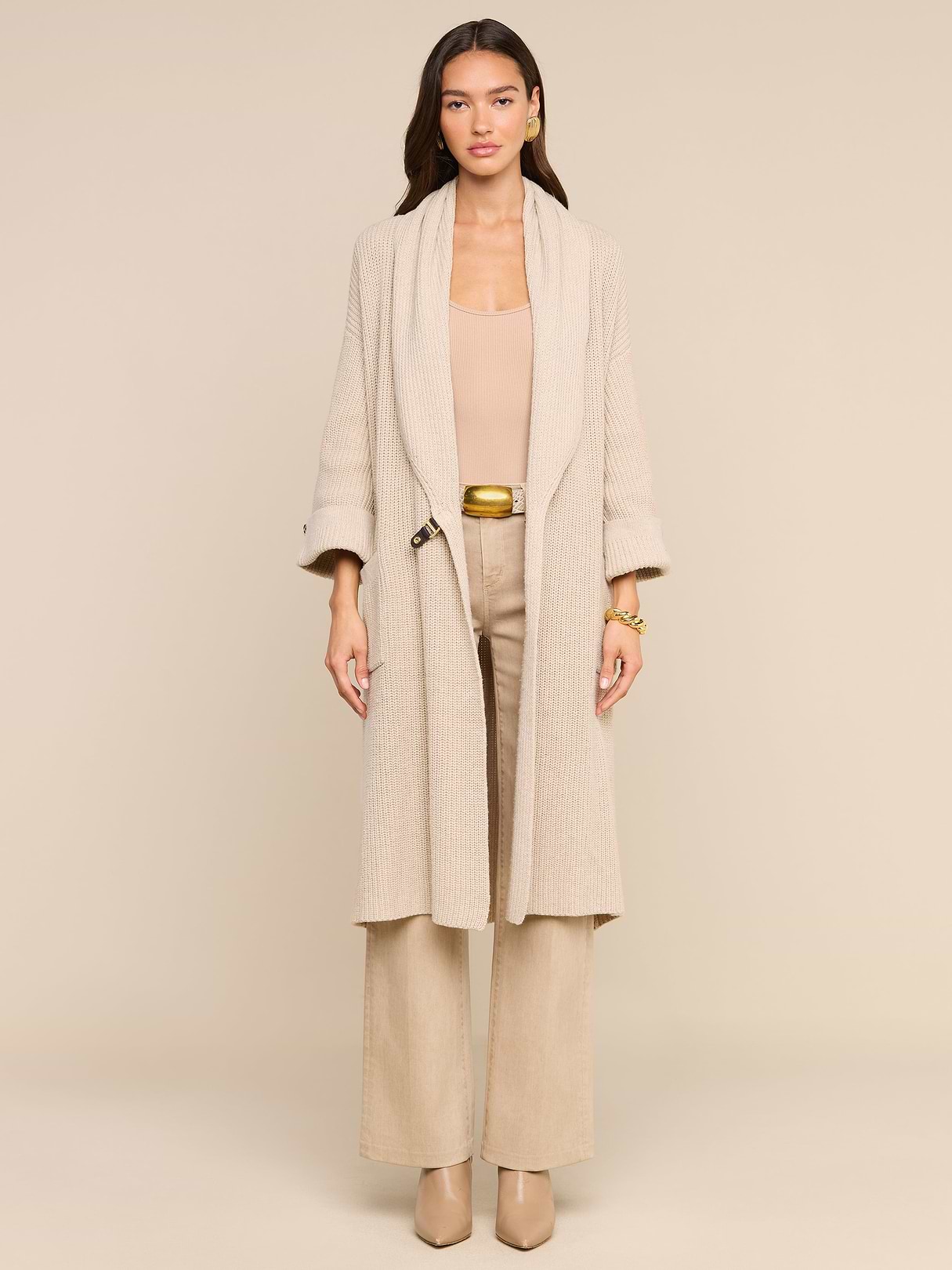 A woman stands facing forward against a plain white background, effortlessly exuding style in the Orielle Cardigan paired with wide-leg pants and heeled shoes, capturing the essence of timeless fall fashion.