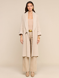 A woman stands facing forward against a plain white background, effortlessly exuding style in the Orielle Cardigan paired with wide-leg pants and heeled shoes, capturing the essence of timeless fall fashion.