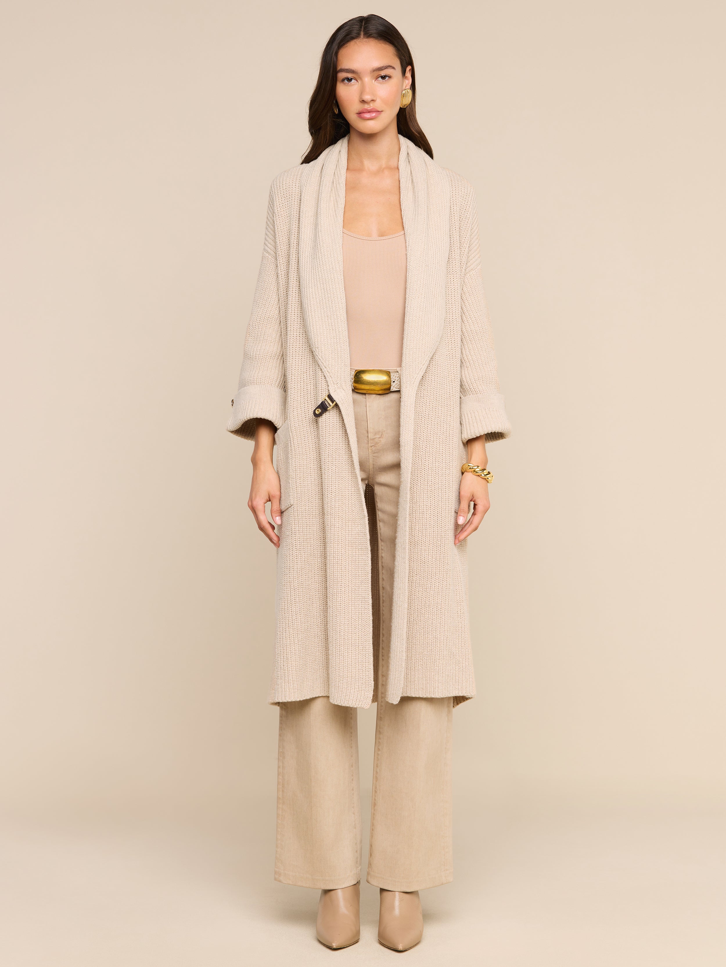 A woman stands facing forward against a plain white background, effortlessly exuding style in the Orielle Cardigan paired with wide-leg pants and heeled shoes, capturing the essence of timeless fall fashion.