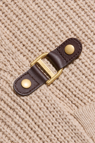 Close-up of a tan knit fabric with a brown leather strap, gold metal D-ring, and gold rivets attached as a decorative or functional detail—perfect for adding a touch of elegance to your favorite Orielle Cardigan.