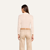 A woman stands with her back to the camera, wearing the Airy Cable Knit Sweater in a light hue and beige pants against a plain light background. Her straight brown hair is down, and her hands rest relaxed at her sides.