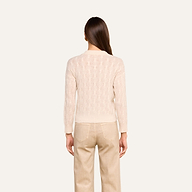 A person with long brown hair stands facing away, wearing the Airy Cable Knit Sweater in a cream shade and beige pants against a plain light background.