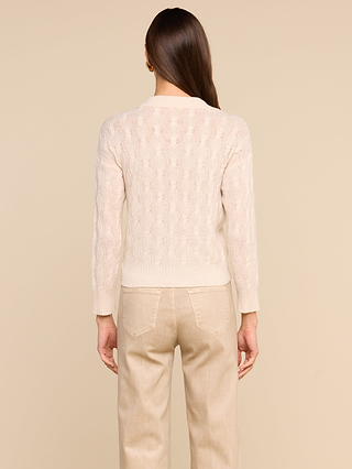 شخص ذو شعر بني طويل، يرتدي سترة «Airy Cable Knit» ذات الياقة العالية، مع بنطال بيج فاتح، يقف وظهره إلى الكاميرا أمام خلفية بيج سادة.