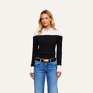 A woman with long blonde hair wears the Mathilde Poplin Collar Pullover—a black off-the-shoulder sweater featuring a white collar and cuffs—paired with blue jeans, a black belt with a gold buckle, and gold earrings, standing against a plain light background.