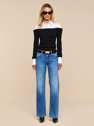 A woman wearing sunglasses, the Mathilde Poplin Collar Pullover, blue jeans, and black shoes stands facing forward against a beige background.
