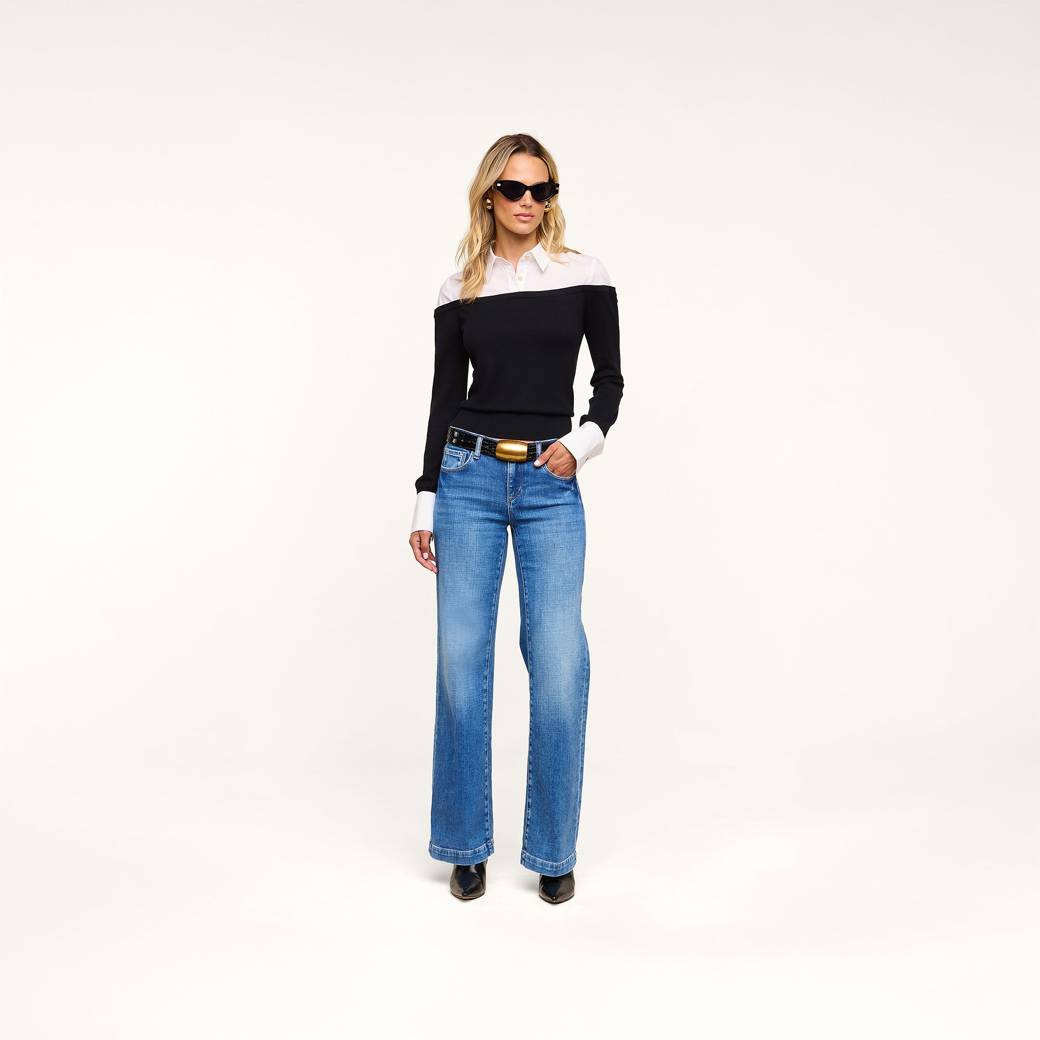 A woman in sunglasses wears the Mathilde Poplin Collar Pullover, styled with blue wide-leg jeans and black shoes, standing against a plain white background.