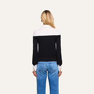 A woman stands facing away, wearing the Mathilde Poplin Collar Pullover—featuring a black and white design with white collar and cuffs—paired with blue jeans, set against a plain light background.