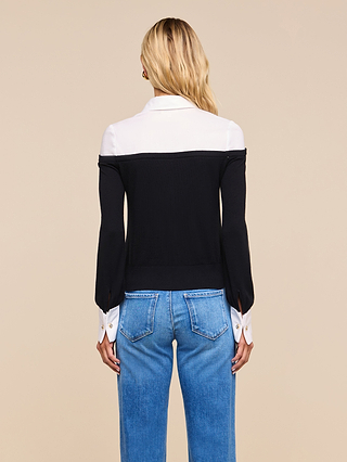 A woman with long blonde hair faces away, wearing the Mathilde Poplin Collar Pullover in black and white with blue jeans, set against a plain beige background.