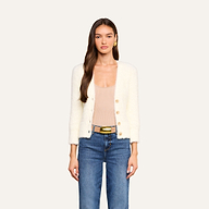 Una donna che indossa il cardigan Agathe sopra un top beige con scollo a V, abbinato a jeans blu, una cintura larga con fibbia dorata e orecchini dorati, è in posa davanti a uno sfondo beige a tinta unita.