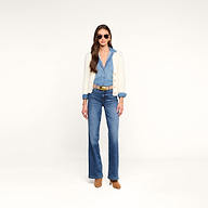 Una donna con indosso occhiali da sole, il cardigan “Agathe”, una tuta in denim con una cintura beige e scarpe con tacco color cuoio è in piedi davanti a uno sfondo beige a tinta unita, con lo sguardo rivolto in avanti e le mani lungo i fianchi.