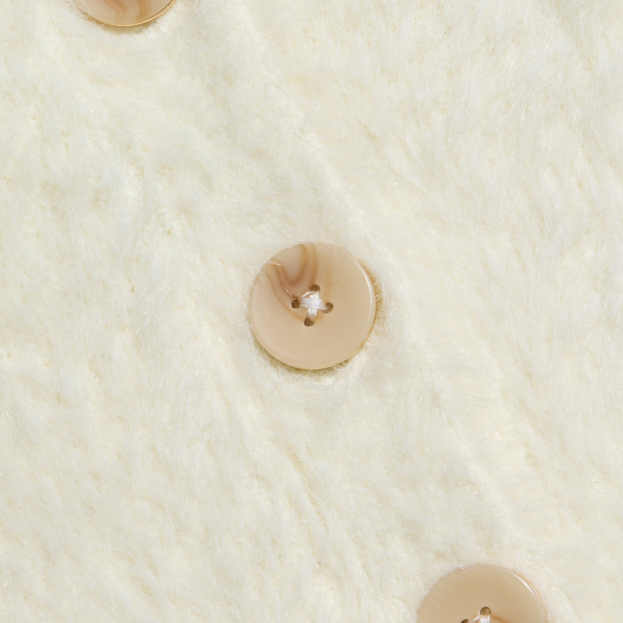 Close-up of three beige buttons with a subtle marbled pattern, sewn in a vertical line onto the soft, cream-colored fuzzy fabric of the Agathe Cardigan Top.