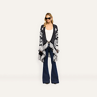 A person in a black and white patterned Naiad Jacquard Fringe Cardigan, white tank top, and relaxed-fit dark blue flared jeans.