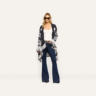 A woman wears a relaxed-fit, boho-chic black and white Naiad Jacquard Fringe Cardigan over a white tank top and flared blue jeans.
