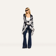 A woman wearing a black and white patterned Naiad Jacquard Fringe Cardigan over a white tank top and dark blue flare jeans.