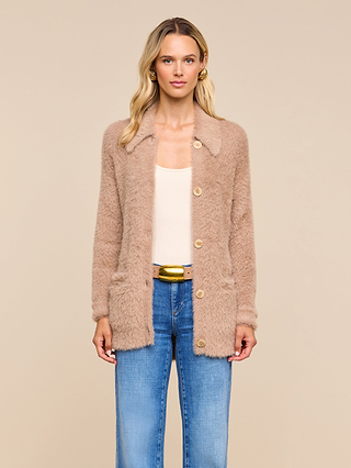 A woman wearing the Mist Cardigan—a cozy, beige fuzzy layer—over a cream top and blue jeans, stands against a plain beige background, facing forward with a neutral expression.
