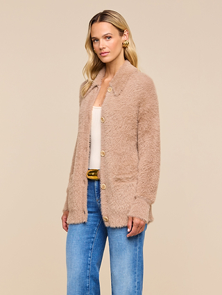 A woman wearing the Mist Cardigan, a soft, fuzzy beige button-up, paired with a cream top and blue jeans stands against a plain beige background.