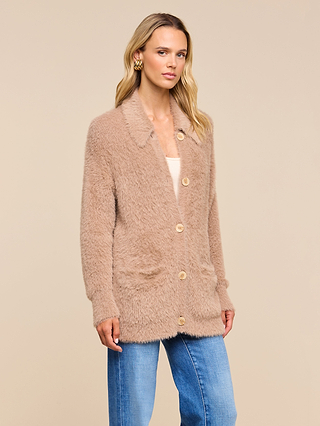 A woman wearing the Mist Cardigan—a soft, beige fuzzy cardigan with buttons—along with blue jeans and gold hoop earrings stands against a plain beige background.