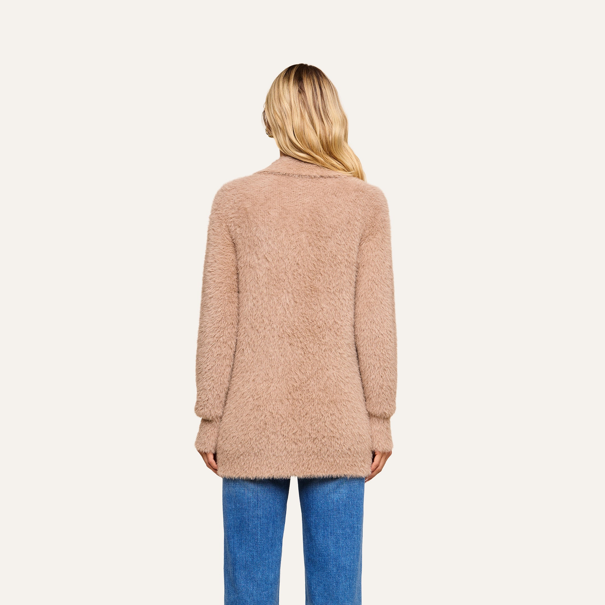 Wearing the Mist Cardigan, a person with long blonde hair and blue jeans is seen from behind, standing against a plain light background. The ultra-soft knit of the cozy sweater adds comfort to their look.