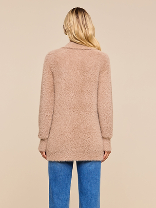 A person with long blonde hair, seen from behind, wears the Mist Cardigan—a cozy light brown oversized style—paired with blue jeans against a plain beige background.