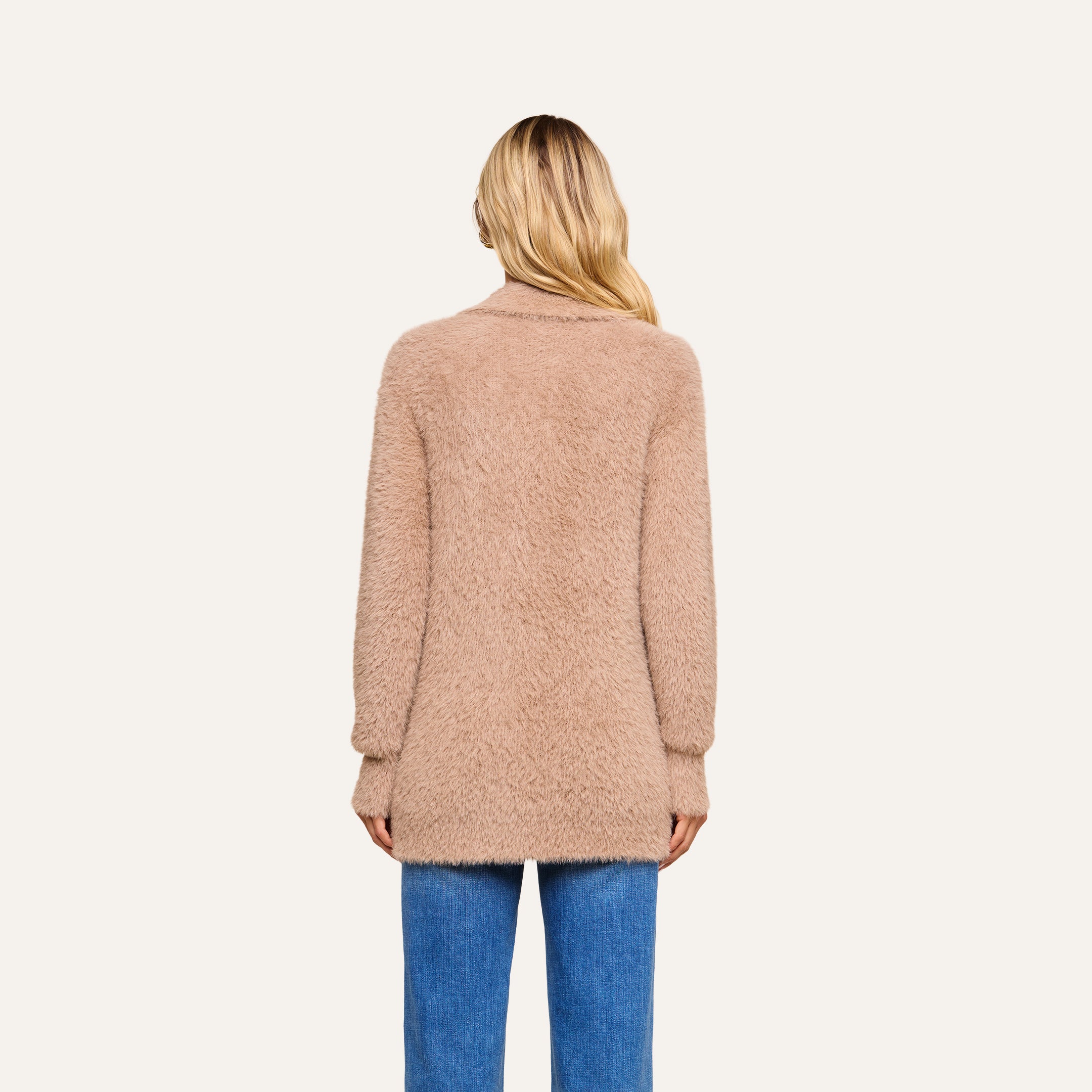 Wearing the Mist Cardigan, a person with long blonde hair and blue jeans is seen from behind, standing against a plain light background. The ultra-soft knit of the cozy sweater adds comfort to their look.