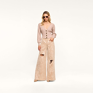 A woman wearing sunglasses, the Hail Cabled Cardigan—a beige cropped cardigan with blouson sleeves and buttons—and wide-legged, textured beige pants with ripped knees stands against a plain white background.