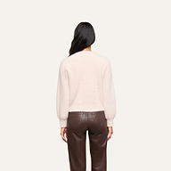 A person with long dark hair is shown from the back, wearing the Nimbus Pullover, a relaxed fit cream-colored fuzzy sweater with balloon sleeves, paired with high-waisted brown leather pants and standing against a plain light background.