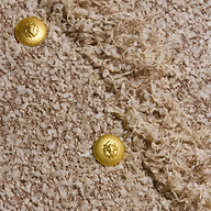 Close-up of the Mireille Fringe Cardigan’s textured beige confetti knit fabric, featuring two shiny gold lion’s head buttons and diagonal sections of smooth and fringed detailing.