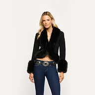 The Irma Cardigan, a cropped black Y2K style with faux fur trim on the collar and cuffs, worn over a denim belt with a large metal buckle and dark blue jeans.