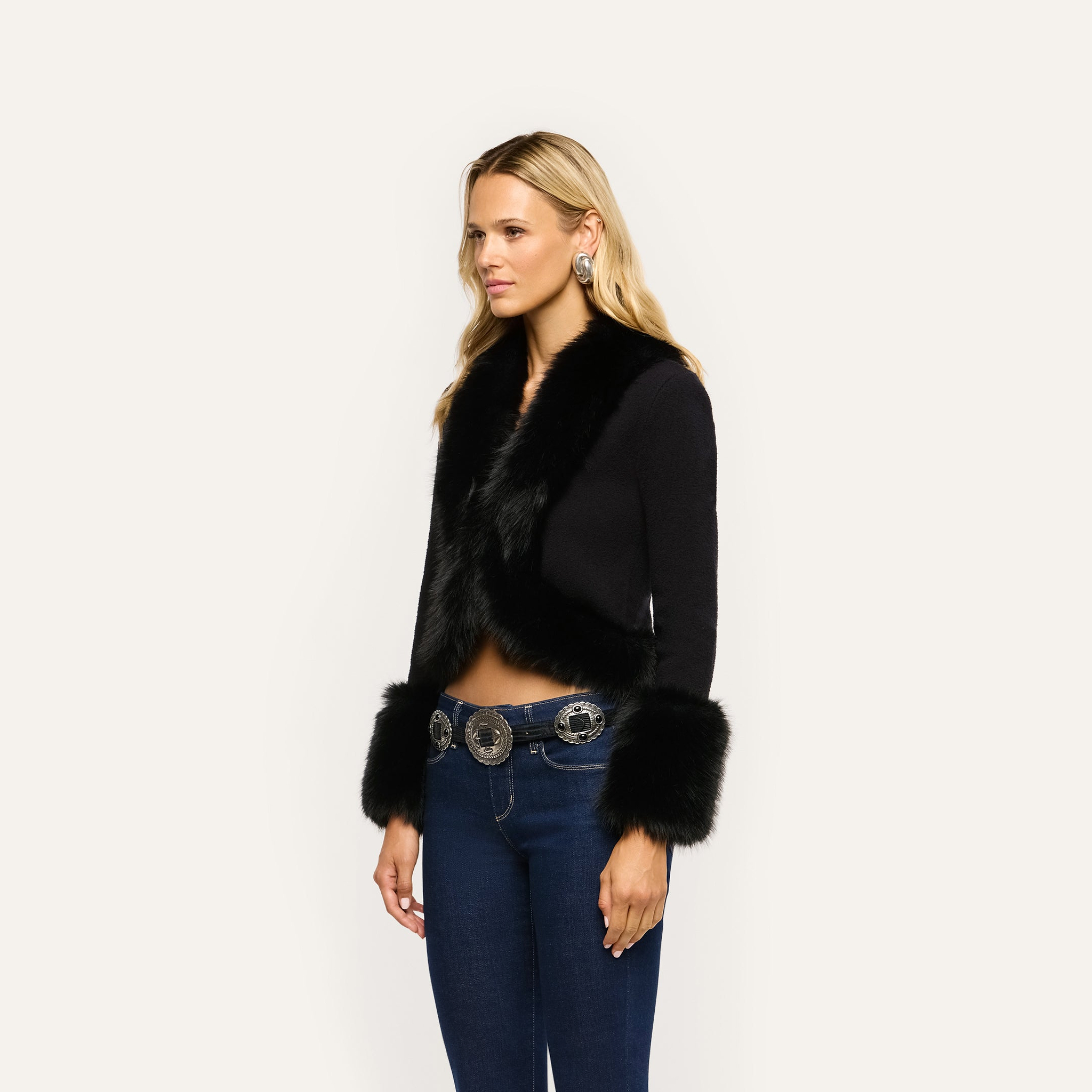 Irma Cardigan, a cropped black Y2K style with faux fur trim on the collar and cuffs, worn with dark blue jeans and a silver concho belt.