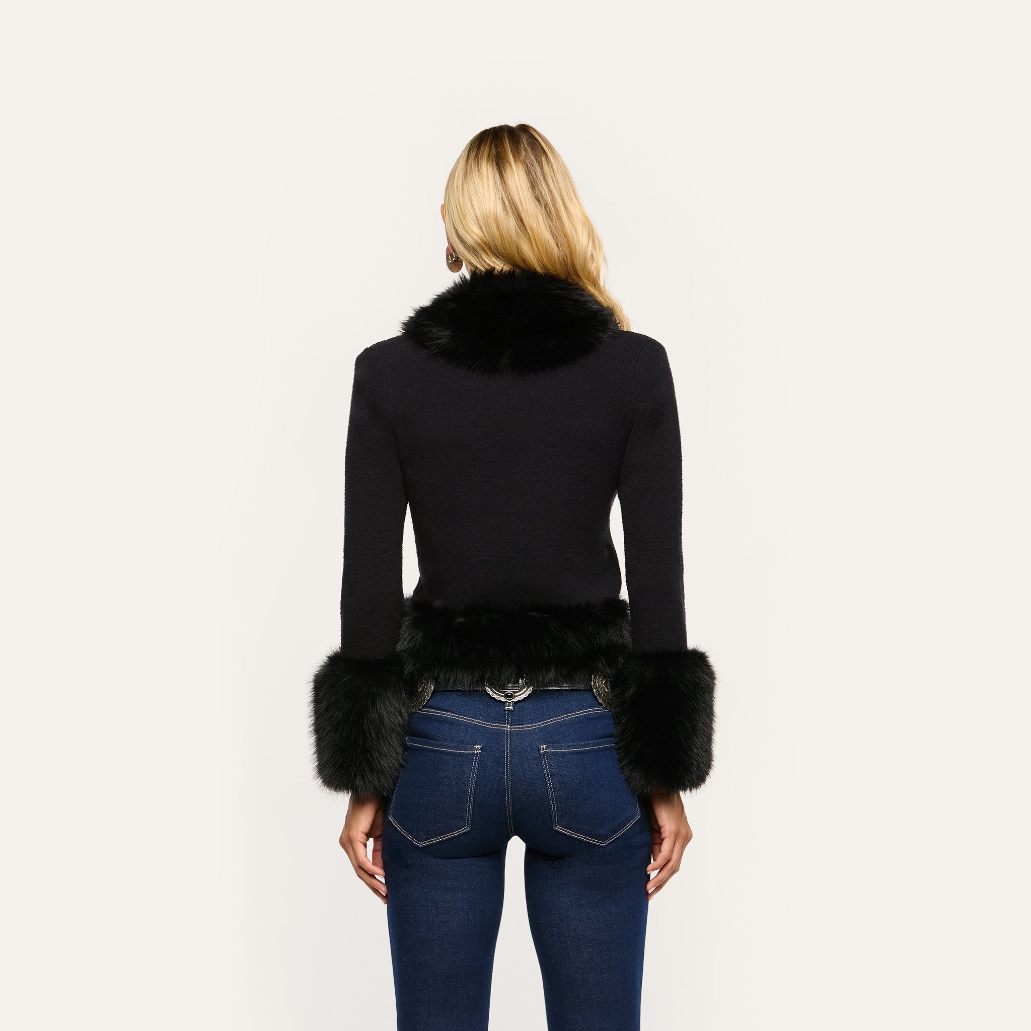 Back view of a person wearing a cropped black Y2K Irma Cardigan with black faux fur trim on the collar and cuffs, paired with dark blue jeans.