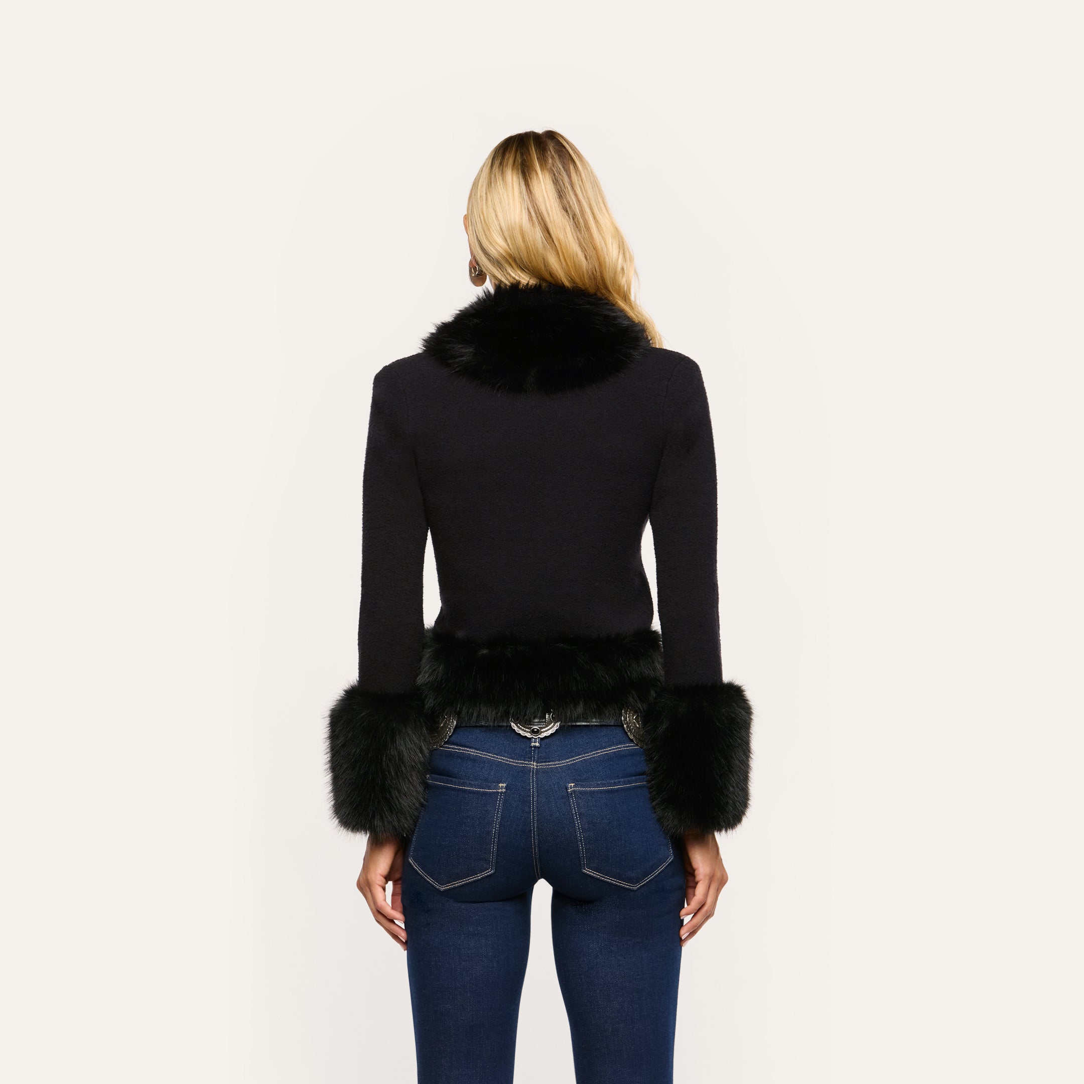 Back view of a person wearing a cropped black Y2K Irma Cardigan with black faux fur trim on the collar and cuffs, paired with dark blue jeans.