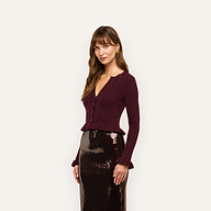 A woman wearing a dark maroon, lightweight, cropped ribbed-knit Finian Cardigan Top with long sleeves, a V-neck, and ruffled hems, paired with a shimmering dark brown sequin skirt.