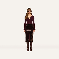 A woman wears a lightweight, ribbed burgundy Finian Cardigan Top with a ruffled hem, a dark sequined midi skirt, and knee-high boots.