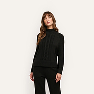 A person wearing the Sandrina Turtleneck, a relaxed-fit, black long-sleeved sweater featuring a central cable-knit pattern.