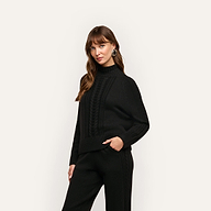 A woman wears the black Sandrina Turtleneck in a relaxed fit with a cable-knit pattern on the front and matching knit trousers.