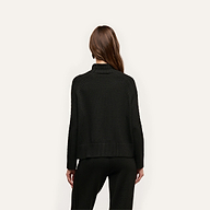 Back view of a person wearing a relaxed fit black cable knit Sandrina Turtleneck.