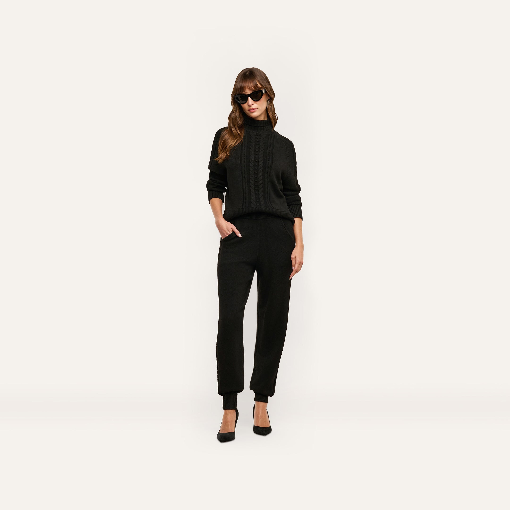 A person wears a black cable-knit sweater and matching Tamaris Cable Knit Pant with black heels and sunglasses.