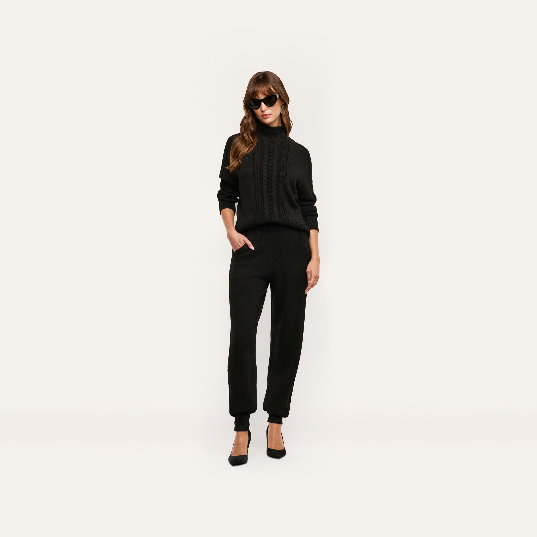 A person wears a black cable-knit sweater and matching Tamaris Cable Knit Pant with black heels and sunglasses.